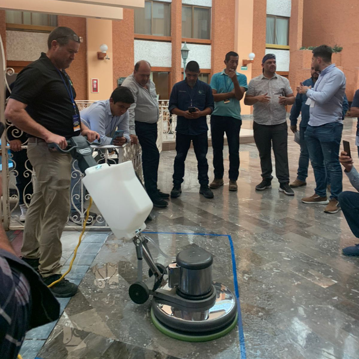 In-house training . Person using a floor polisher on a large stone surface with onlookers in a hotel lobby