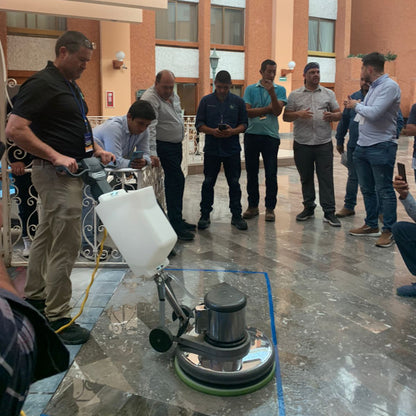 In-house training . Person using a floor polisher on a large stone surface with onlookers in a hotel lobby